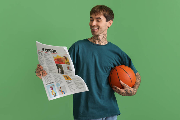 Gelukkig jongeman met bal voor basketbal en krant op groene achtergrond - Foto, afbeelding