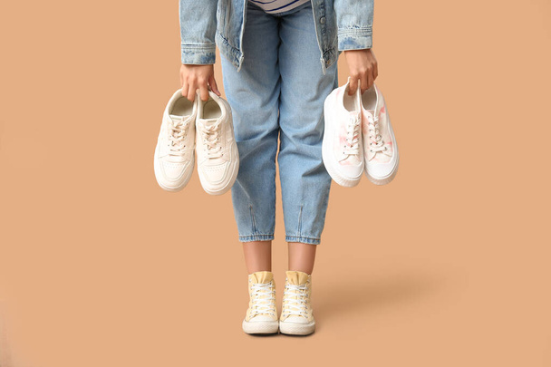 Pernas de jovem mulher em tênis elegantes segurando sapatos diferentes no fundo bege - Foto, Imagem