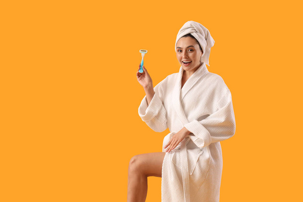 Gyönyörű fiatal boldog nő fürdőköpenyben borotvával sárga háttér - Fotó, kép