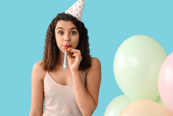Mooie jonge vrouw met feest fluitje en luchtballonnen vieren verjaardag op blauwe achtergrond - Foto, afbeelding