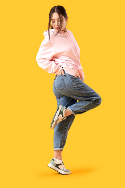 Joven mujer asiática en jeans de moda sobre fondo amarillo - Foto, Imagen