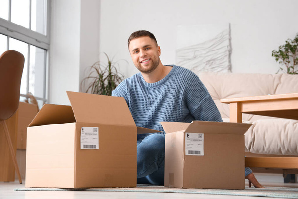 Junger Mann mit Paketen sitzt zu Hause auf dem Boden - Foto, Bild