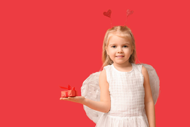 Aranyos kislány Cupidónak öltözve, ajándékdobozzal a piros háttérben. Valentin-napi ünneplés - Fotó, kép