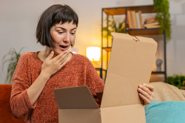Glückliche hispanische junge Frau beim Auspacken von Paketen. Lächelnd zufriedene Shopperin, Online-Shop-Kunde öffnet Karton erhält Einkaufsgeschenk durch schnellen Postversand - Foto, Bild