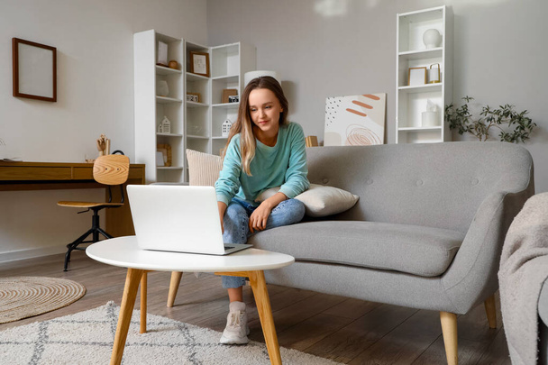 Jeune femme sur canapé gris en utilisant un ordinateur portable dans le salon - Photo, image