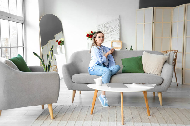 Piękna młoda kobieta siedzi na szarej kanapie w salonie - Zdjęcie, obraz