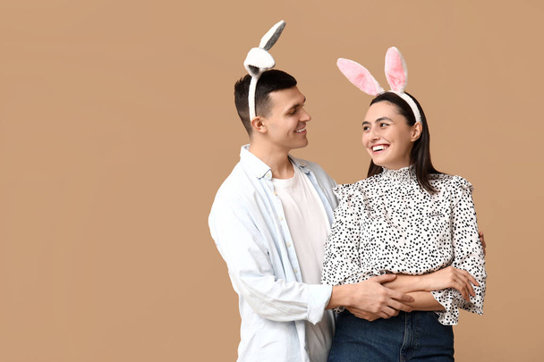Ευτυχισμένο νεαρό ζευγάρι με αυτιά πασχαλινού κουνελιού σε μπεζ φόντο - Φωτογραφία, εικόνα