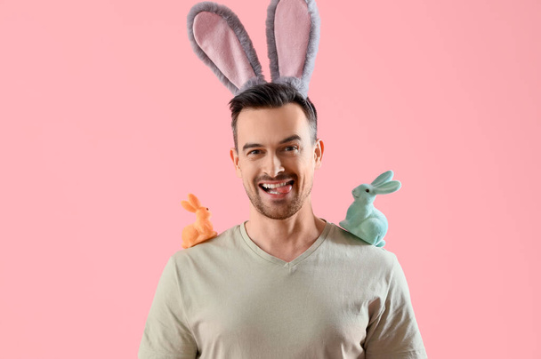 Joyeux jeune homme aux oreilles de lapin avec des lapins de Pâques sur fond rose - Photo, image