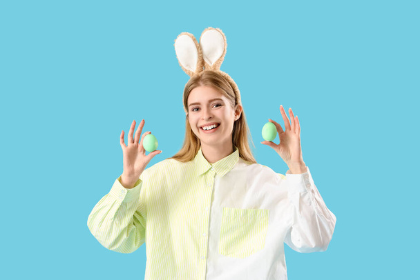 Mladá žena v králičí uši s velikonočními vejci na modrém pozadí - Fotografie, Obrázek