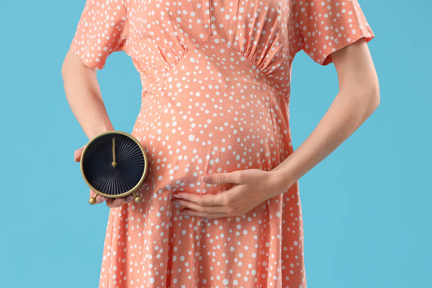 Jovem grávida com despertador no fundo azul, close-up - Foto, Imagem