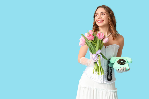 Молода жінка з ретро телефоном і букетом красивих тюльпанів на синьому фоні. Міжнародний жіночий день - Фото, зображення