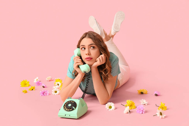 Jonge vrouw praten door retro telefoon met mooie bloemen op roze achtergrond. Internationale Vrouwendag - Foto, afbeelding
