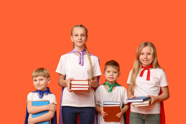 Nette Kinder im Superheldenkostüm mit Büchern auf orangefarbenem Hintergrund. Tag der Bücherfreunde - Foto, Bild