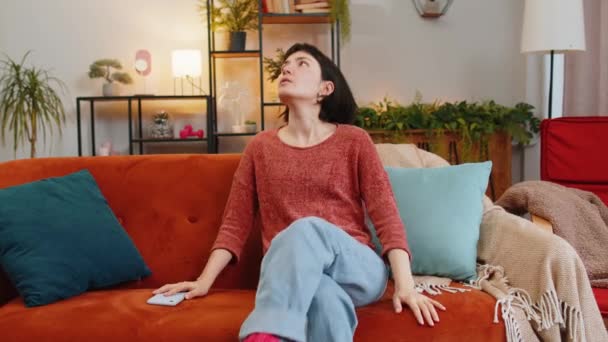 Irritated Caucasian woman girl covers ears with cushions, annoyed by noisy neighbors suffers from headache sitting on sofa. Thin walls at home, flat without sound insulation, repair work concept. - Footage, Video