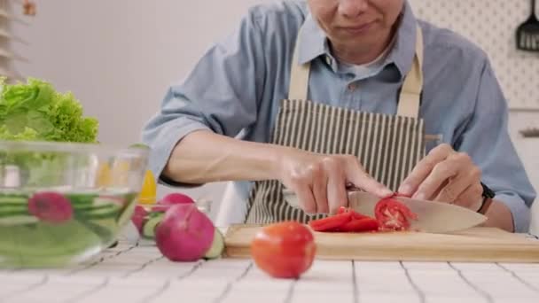 Vidám középkorú férfi paradicsomot vág a fedélzeten, egészséges vegán salátát készít a konyhában.. - Felvétel, videó