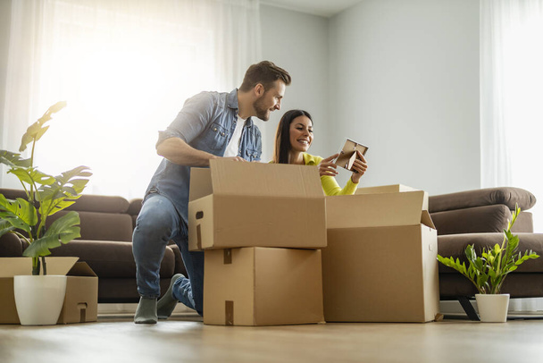 Glückliches junges Ehepaar zieht in neue Wohnung und packt Kisten aus.Lächelndes Paar packt Kisten im neuen Zuhause aus. - Foto, Bild