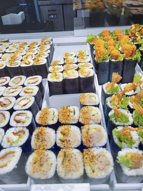 Sushi na výloze na trhu s potravinami. Sushi je japonské jídlo z připravené octové rýže, obvykle s trochou cukru a soli, doplněné různými složkami, jako jsou mořské plody a zelenina. - Fotografie, Obrázek