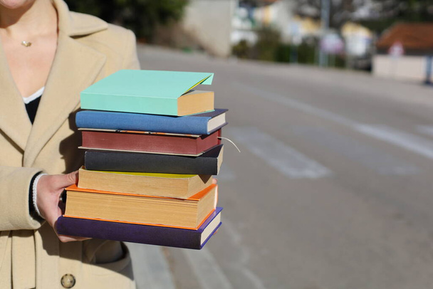 Μια γυναίκα που κρατάει μια στοίβα βιβλία στα χέρια της. - Φωτογραφία, εικόνα