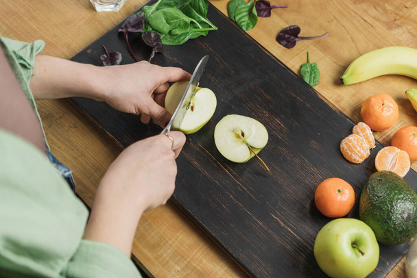Elma kesen kadın, masada ıspanak yapraklı, muzlu ve avokadolu sağlıklı vejetaryen smoothie hazırlıyor.. - Fotoğraf, Görsel
