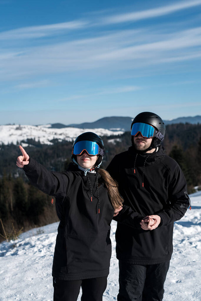 Een getrouwd stel is aan het skiën in de bergen. Een man en een vrouw skiërs poseren tegen de achtergrond van besneeuwde bergen. Het concept van skiën - Foto, afbeelding