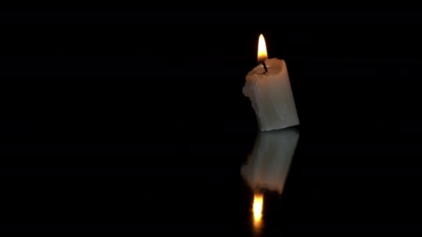 短いパラフィンキャンドルが黒い背景に反射して燃える. 1つのライトキャンドルは暗い背景に対して明るいオレンジ色の炎で燃えます. 悲しみの象徴,死者の記憶,戦争の概念. - 映像、動画