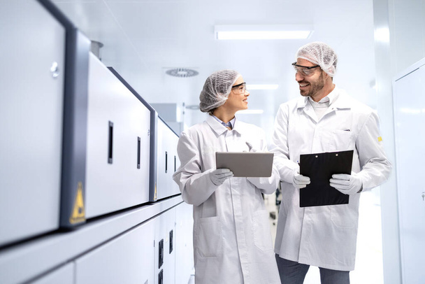 Travailleurs pharmaceutiques debout près de la machine de ligne de production et contrôlant la qualité dans des conditions de travail stériles. - Photo, image