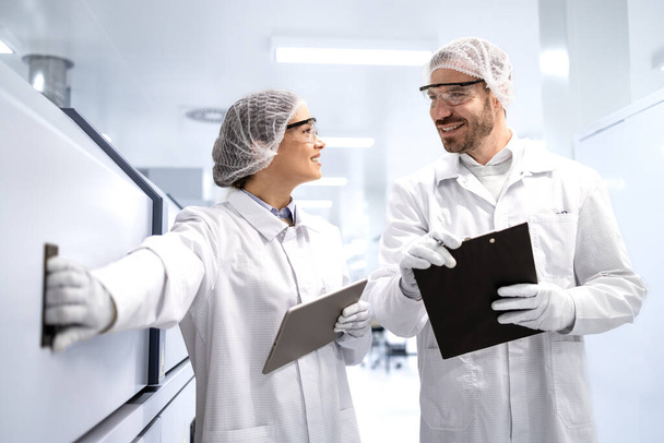 Фармацевтичні працівники в білому пальто і шершнях перевіряють виробництво ліків всередині заводу. - Фото, зображення