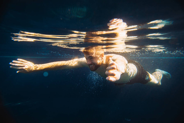 Un beau jeune homme nage sous l'eau dans une piscine pendant ses vacances. - Photo, image