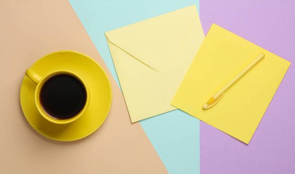 Gelbe Kaffeetasse und Umschlag aus Keramik auf pastellfarbenem Hintergrund. Ansicht von oben - Foto, Bild