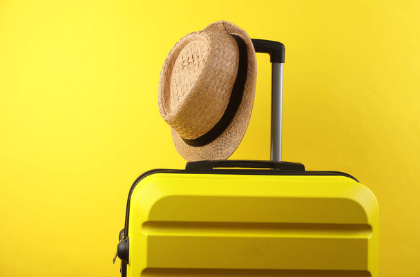 Valise de voyage en plastique jaune avec chapeau sur fond jaune. Bagages, tourisme, vacances, concept de relocalisation - Photo, image
