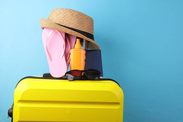 Gele plastic reiskoffer met hoed, paspoort en teenslippers, zonnebrandcrème op een gele achtergrond. Toerisme, zomervakantie, strandresort, relocatieconcept - Foto, afbeelding