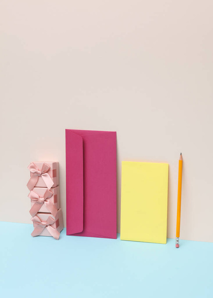 Enveloppe violette avec carte de vœux jaune, coffrets cadeaux et stylo sur fond pastel. Mise en page vacances créatives.  - Photo, image