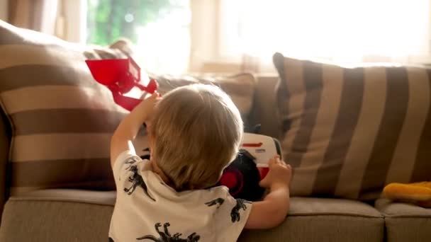 Видеосъемка мальчика, сидящего на диване и сжимающего пару ярких игрушек. - Кадры, видео
