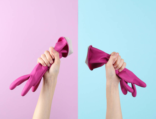 Manos que sostienen guantes de goma rosa para limpiar sobre un fondo pastel azul-rosa - Foto, Imagen