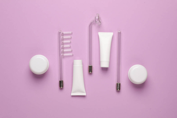 Acne treatment. Nozzles for local darsonvalization with cream jars and tubes on a purple background. Beauty concept. Flat lay - Photo, Image