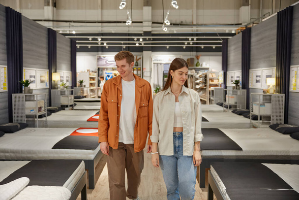 Young man and woman couple looking for new comfortable bed at modern furniture shop. Family shopping time concept - Photo, Image