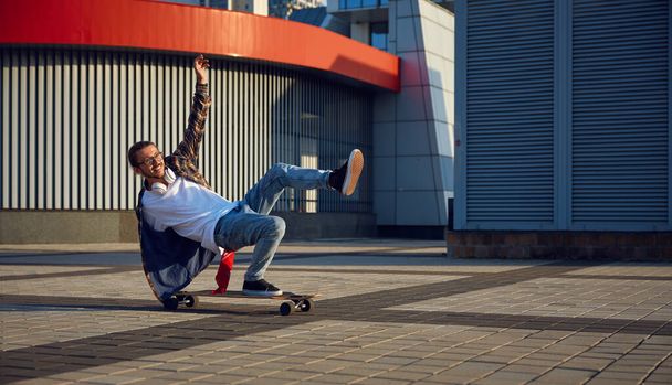 Excité hipster gars habile faisant cascade sur skateboard équitation rapide sur la rue urbaine. Patineur adolescent habillé à la mode faisant un tour de main. Sport hobby des jeunes concept - Photo, image