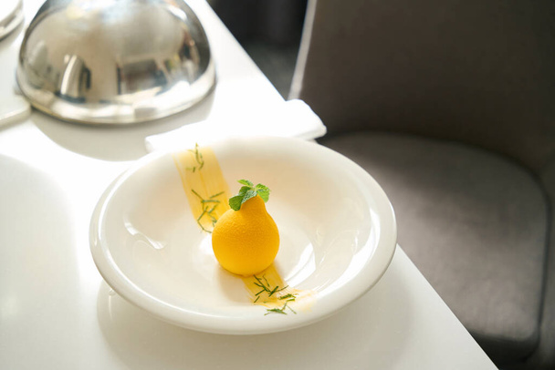 Exquisito postre se sirve con hojas de menta en plato blanco, tapa de cloche se encuentra junto a ella en la mesa de servir - Foto, Imagen