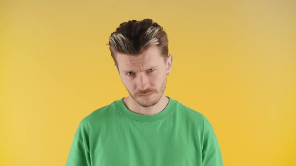 Een man met stoppels en een stijlvolle kapsel staart in de camera. Een serieuze jongeman in een groen t-shirt staat op een gele achtergrond en kijkt continu naar de camera. Hoge kwaliteit 4k beeldmateriaal - Video