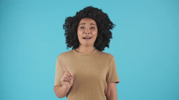 Een vrouw die tegen een blauwe achtergrond staat en met haar vinger zwaait terwijl ze naar de camera kijkt. Jonge zwarte vrouw zwaait met haar vinger in ontkenning. Hoge kwaliteit 4k beeldmateriaal - Video