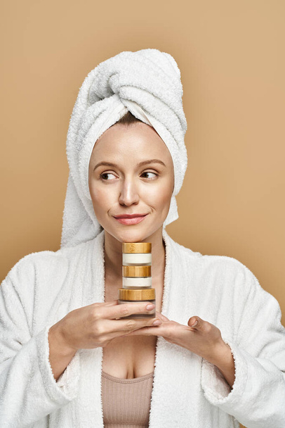 Uma mulher serena com uma toalha na cabeça segurando um frasco de creme, mostrando beleza natural e rotina de autocuidado. - Foto, Imagem