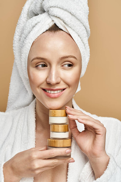Μια γυναίκα με μια πετσέτα στο κεφάλι της με χάρη κρατά κρέμα, ενσωματώνοντας χαλάρωση και κομψότητα. - Φωτογραφία, εικόνα