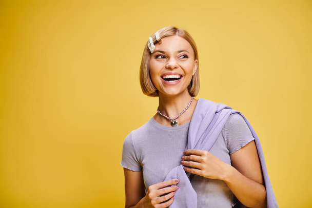 happy well dressed woman with blonde short hair in vibrant attire posing on yellow backdrop - Photo, Image
