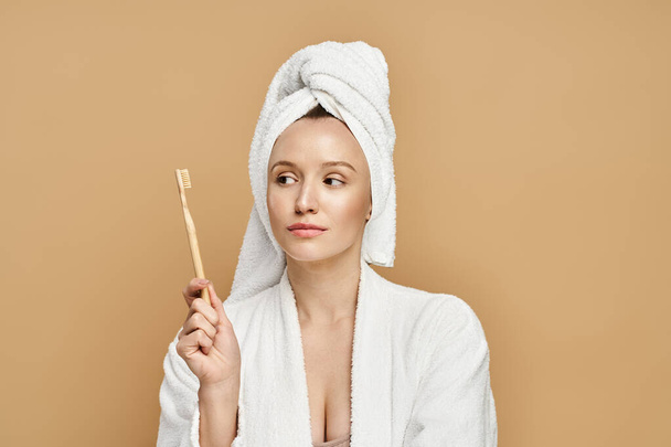 Μια γυναίκα με μια πετσέτα στο κεφάλι της με χάρη κρατά μια βούρτσα, αναδεικνύοντας τη φυσική ομορφιά και λάμψη της. - Φωτογραφία, εικόνα