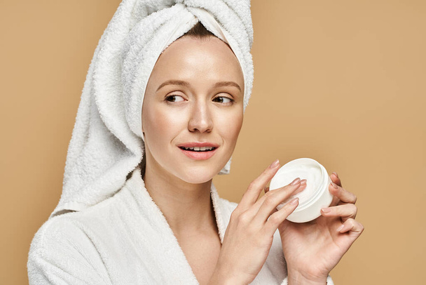 Una donna di bellezza naturale tiene un barattolo di crema con un asciugamano in testa. - Foto, immagini