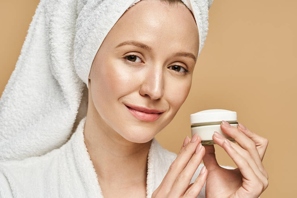 A woman with a towel on her head holds a jar of cream, embracing self-care and natural beauty. - Photo, Image