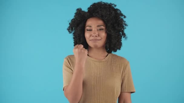 Une fille noire se tient devant la caméra et agite le poing. Une jeune femme noire debout sur un fond bleu menace de montrer son poing à la caméra. Images 4k de haute qualité - Séquence, vidéo