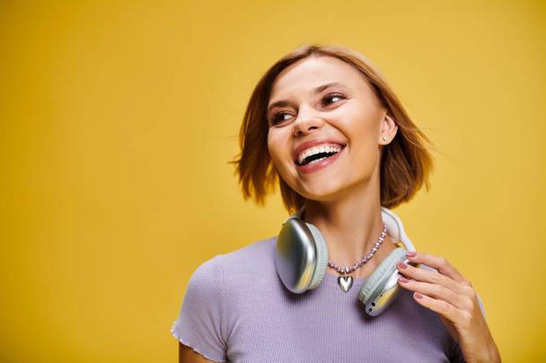 graceful joyous woman with short blonde hair and headphones enjoying music on yellow backdrop - Photo, image