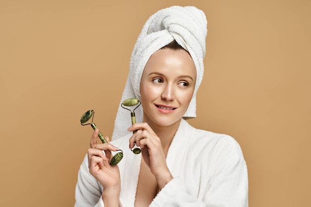 Una donna con un asciugamano sulla testa tiene rullo viso, mostrando la sua bellezza naturale e il collegamento con la natura. - Foto, immagini