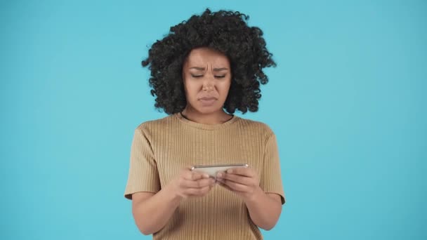 若い女性がカメラの前に立ってスマホで遊んでいる。モバイルゲームでレベルを失敗した後、アフリカ系アメリカ人の女性が頭を震わせていた。高品質4k映像 - 映像、動画
